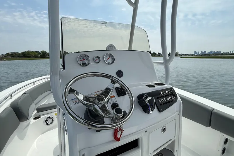Slide: The Image of 2025 NauticStar 212 Legacy boat dashboard with steering wheel and controls on a calm water backdrop. - 22