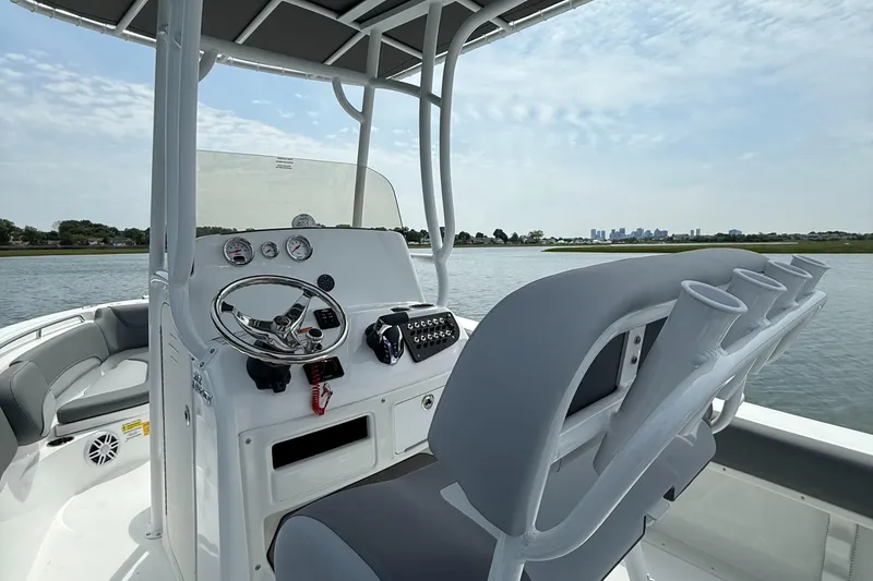 Slide: The Image of 2025 NauticStar 212 Legacy boat interior with steering console and seating on a calm waterway. - 23