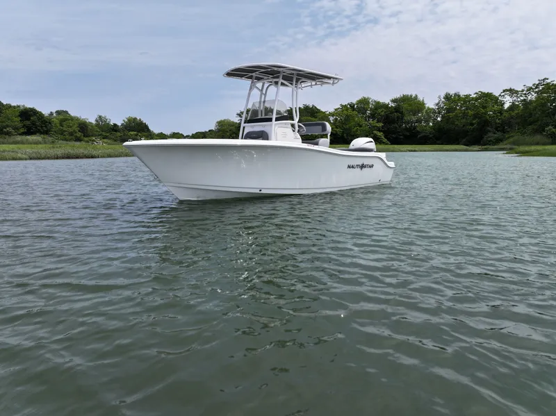 Slide: The Image of 2025 NauticStar 212 Legacy boat on calm water, surrounded by lush greenery. - 7