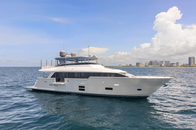 Slide: The Image of 2019 Hatteras M90 Panacera yacht cruising on open sea with city skyline backdrop. - 0