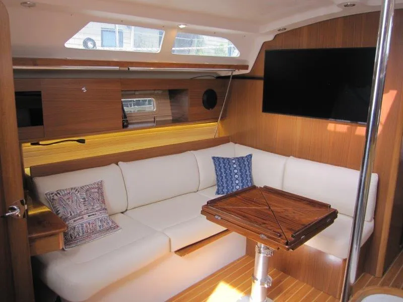 Slide: The Image of 2024 Catalina 385 yacht interior with white seating, wooden table, and mounted TV. - 10