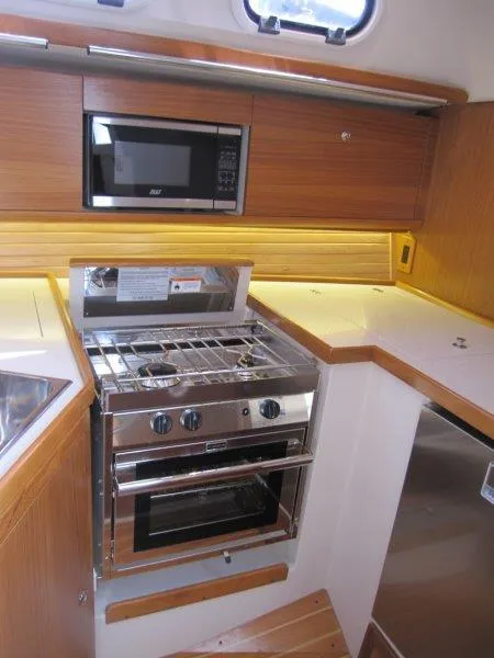 Slide: The Image of 2024 Catalina 385 yacht kitchen with stove, oven, microwave, and wooden cabinetry. - 13