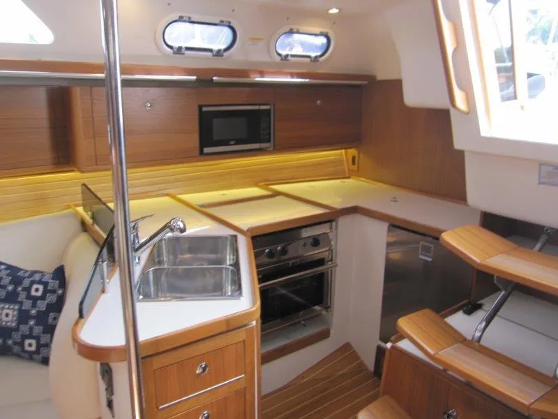 Slide: The Image of 2024 Catalina 385 yacht interior kitchen with wood finish, sink, stove, and microwave. - 7