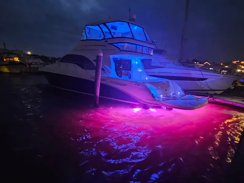 Slide: The Image of Illuminated 2006 Sea Ray 580 Sedan Bridge yacht with vibrant blue and pink lights at night. - 11