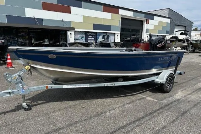 Slide: The Image of 2025 Lund 1675 Alaskan Tiller boat on trailer, parked outside a modern building. - 5