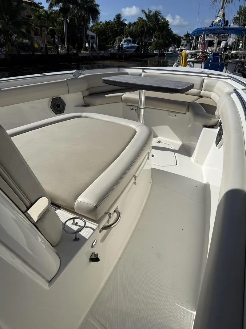 Slide: The Image of 2020 Boston Whaler 330 Outrage boat interior with seating and table, docked near palm trees. - 17