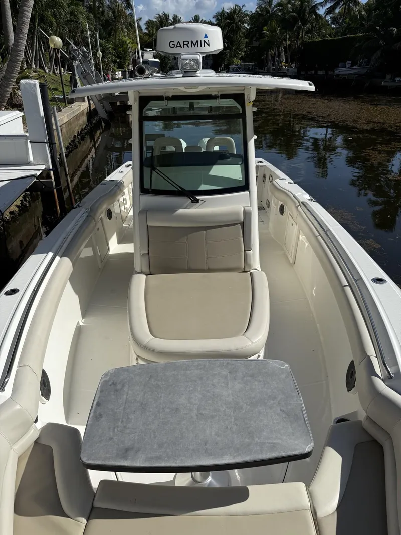 Slide: The Image of 2020 Boston Whaler 330 Outrage boat interior with seating and table, docked by palm trees. - 18