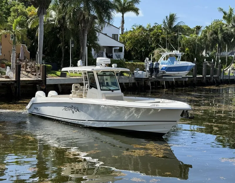 Slide: The Image of 2020 Boston Whaler 330 Outrage boat docked near palm trees and waterfront homes. - 2