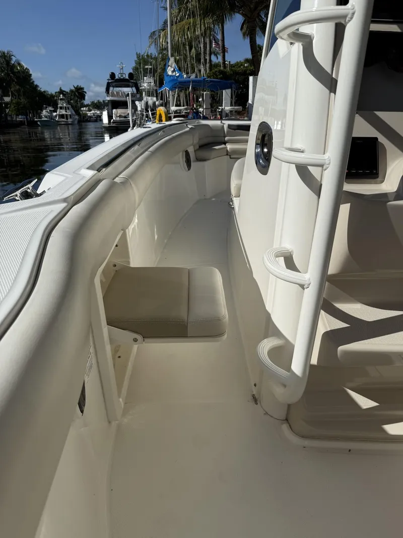 Slide: The Image of 2020 Boston Whaler 330 Outrage boat interior with seating and ladder, docked near palm trees. - 24