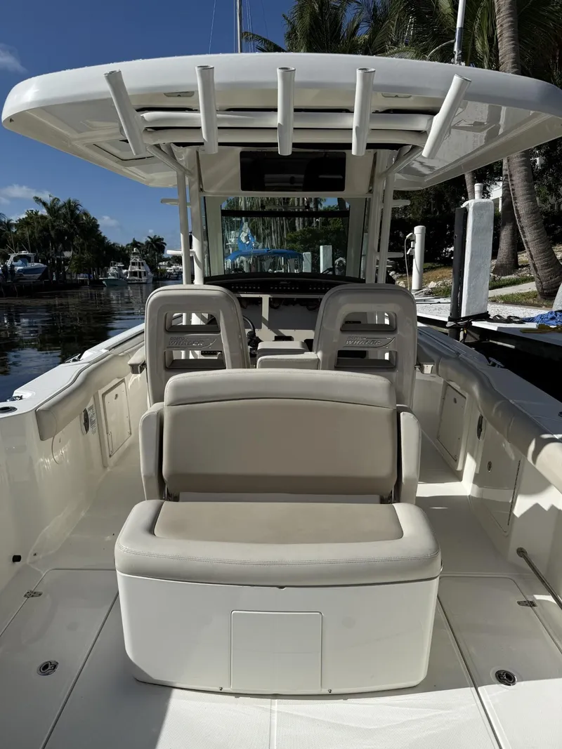 Slide: The Image of 2020 Boston Whaler 330 Outrage boat interior with seating and helm, docked near palm trees. - 28