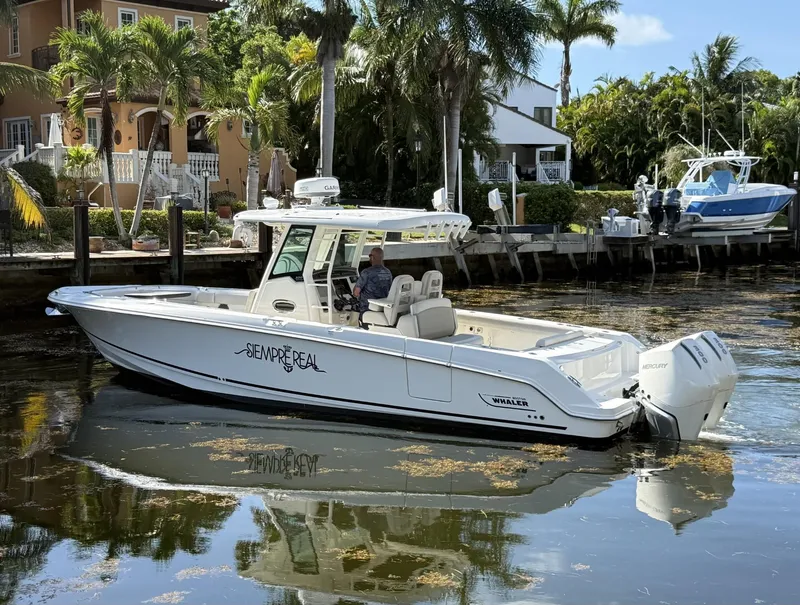 Slide: The Image of 2020 Boston Whaler 330 Outrage boat docked near waterfront homes, surrounded by palm trees. - 6