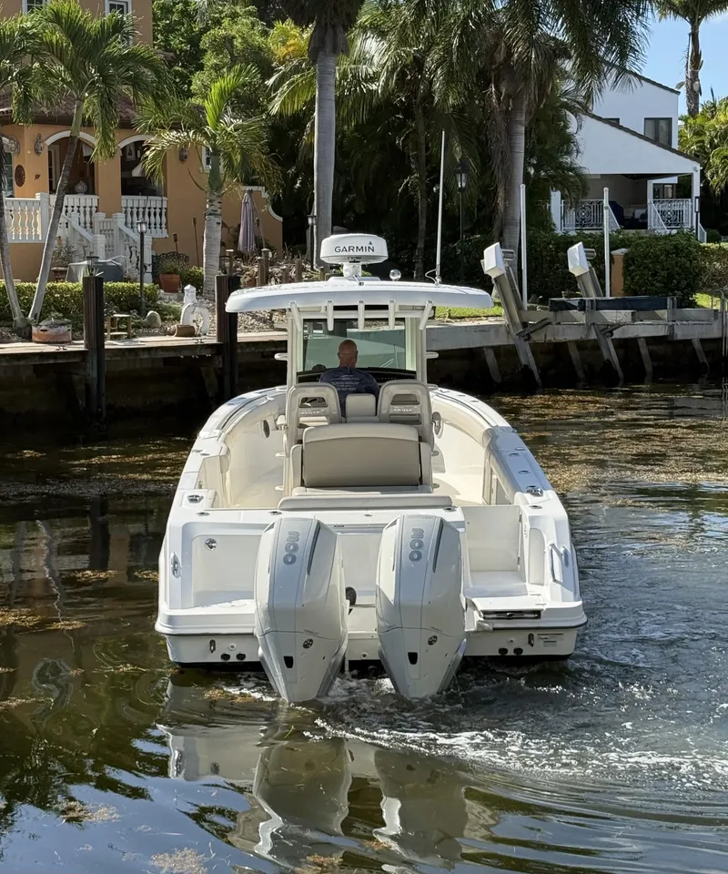 Slide: The Image of 2020 Boston Whaler 330 Outrage boat navigating a canal with palm trees in the background. - 8