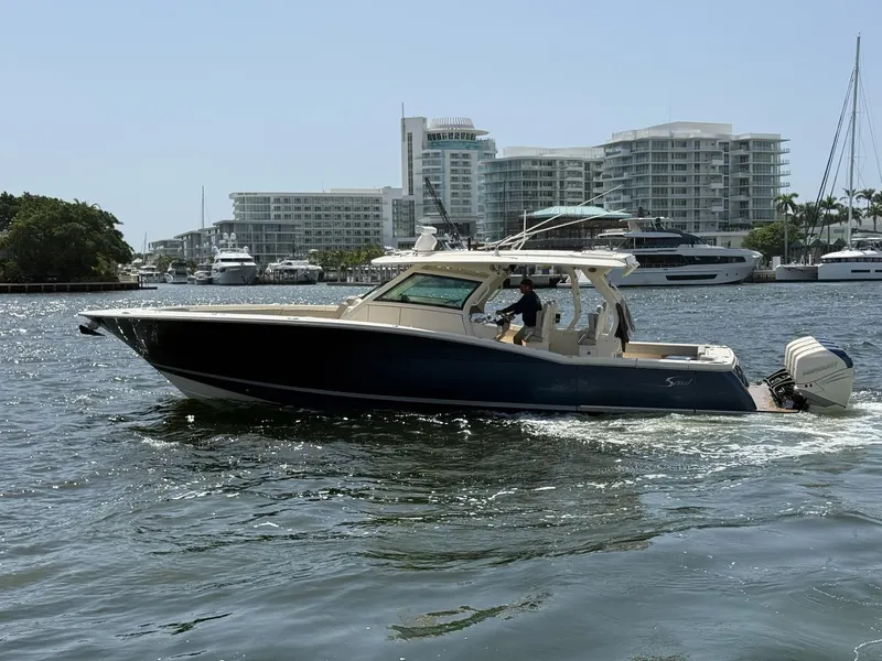 Slide: The Image of 2019 Scout 420 LXF boat cruising in a marina with modern buildings in the background. - 2