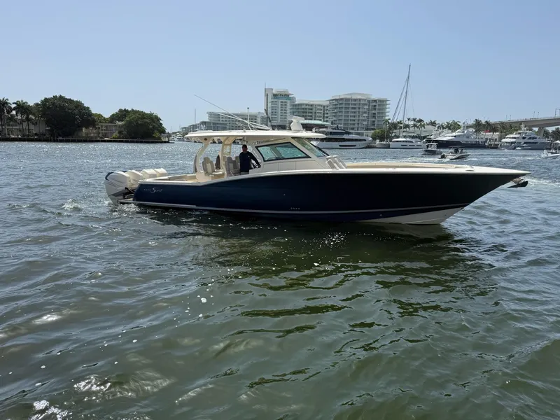 Slide: The Image of 2019 Scout 420 LXF boat cruising in a marina with modern buildings in the background. - 5