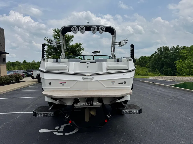Slide: The Image of 2023 MasterCraft XT23 boat parked on asphalt, rear view with speakers and lush greenery. - 4
