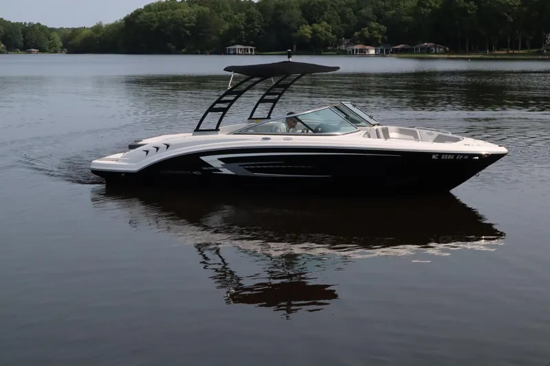 The Image of 2020 Chaparral 23 SSi boat cruising on a calm lake with forested shoreline. - 0