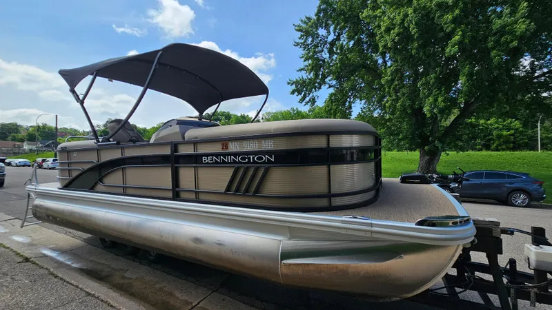 Slide: The Image of 2021 Bennington L 22 Quad Bench pontoon boat on trailer, parked near trees. - 4
