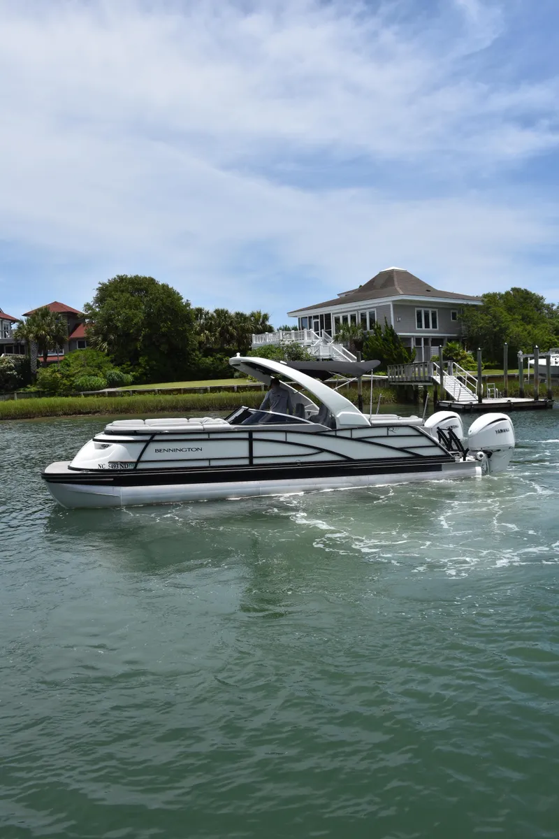 The Image of 2024 Bennington 27 QFB boat cruising on a sunny day near waterfront homes. - 1