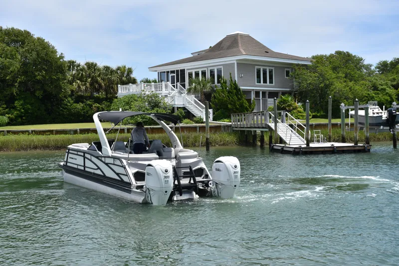 Slide: The Image of 2024 Bennington 27 QFB boat cruising near a waterfront house with lush greenery. - 10