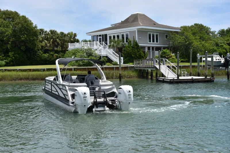 Slide: The Image of 2024 Bennington 27 QFB boat cruising near a waterfront house with lush greenery. - 11
