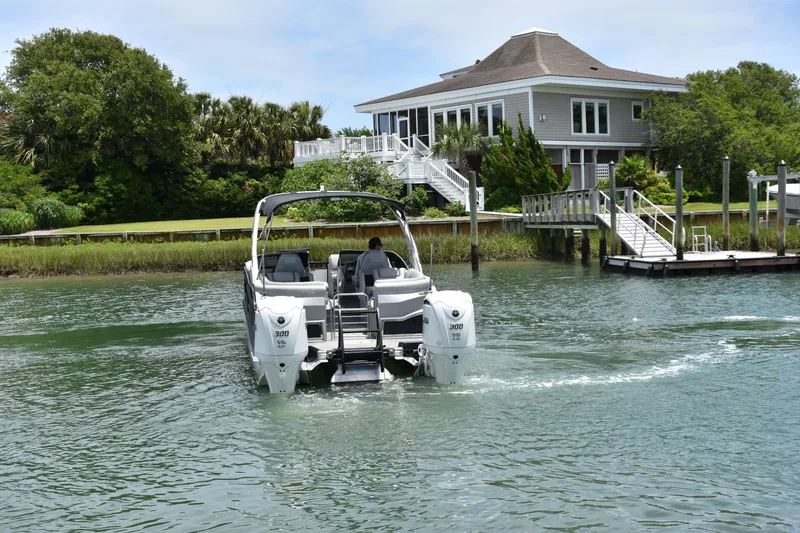 Slide: The Image of 2024 Bennington 27 QFB boat cruising near a waterfront house. - 12