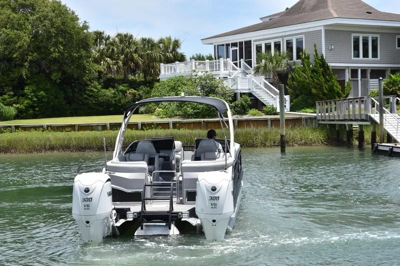 Slide: The Image of 2024 Bennington 27 QFB pontoon boat cruising near a waterfront home. - 13