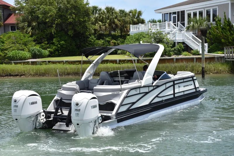 Slide: The Image of 2024 Bennington 27 QFB pontoon boat cruising on a scenic waterway. - 14