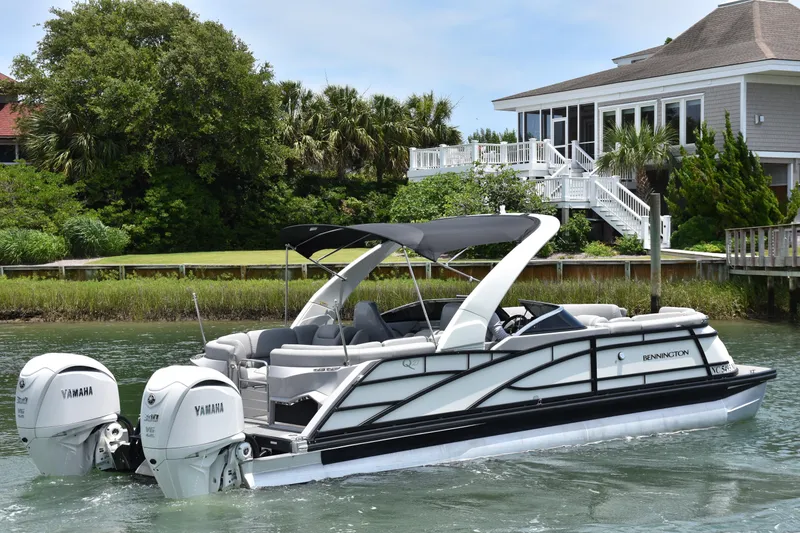 Slide: The Image of 2024 Bennington 27 QFB pontoon boat with Yamaha engines near a waterfront home. - 16