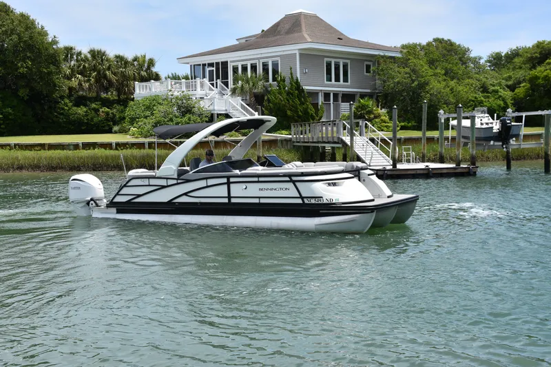 Slide: The Image of 2024 Bennington 27 QFB pontoon boat cruising near a waterfront house. - 19