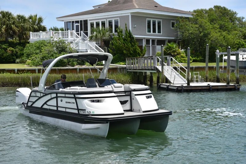 Slide: The Image of 2024 Bennington 27 QFB pontoon boat cruising near a waterfront house. - 20