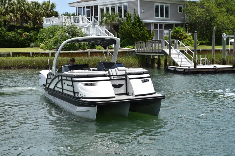 Slide: The Image of 2024 Bennington 27 QFB pontoon boat cruising near a waterfront home. - 21