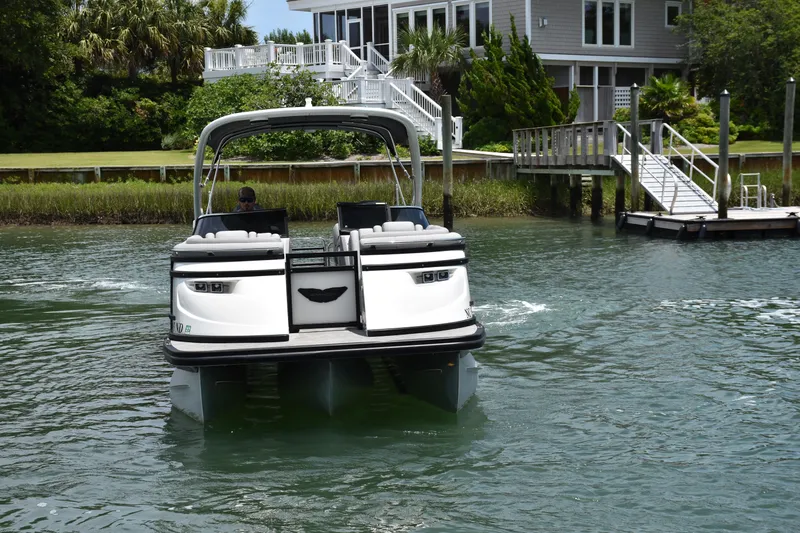 Slide: The Image of 2024 Bennington 27 QFB pontoon boat cruising near a waterfront home. - 22