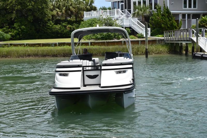 Slide: The Image of 2024 Bennington 27 QFB pontoon boat on water near a dockside house. - 23