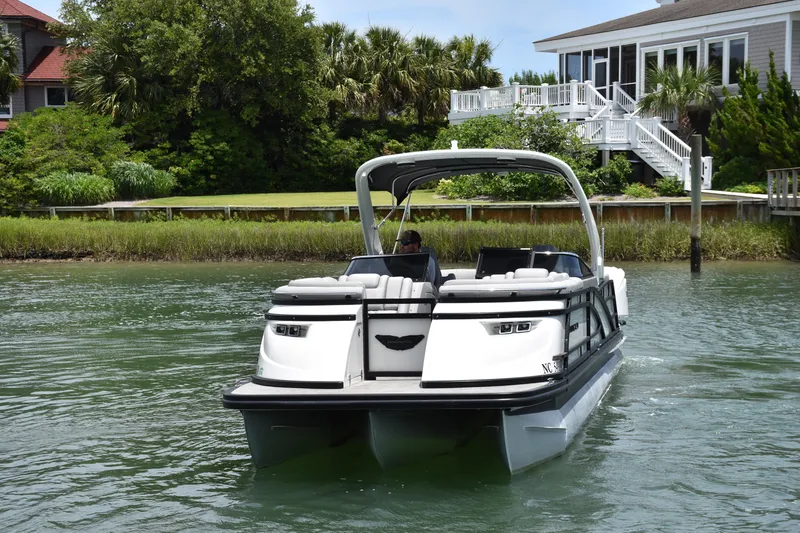 Slide: The Image of 2024 Bennington 27 QFB pontoon boat cruising near a waterfront home. - 24