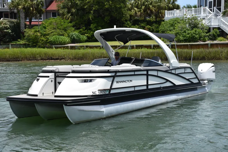 Slide: The Image of 2024 Bennington 27 QFB pontoon boat cruising on a scenic waterway. - 28