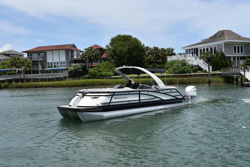 Slide: The Image of 2024 Bennington 27 QFB pontoon boat cruising near waterfront homes. - 29