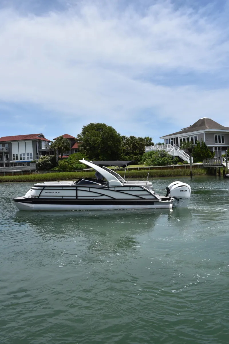 Slide: The Image of 2024 Bennington 27 QFB boat cruising on a calm waterway near waterfront homes. - 3