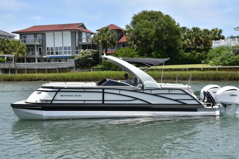 Slide: The Image of 2024 Bennington 27 QFB pontoon boat on water, with modern houses in the background. - 30