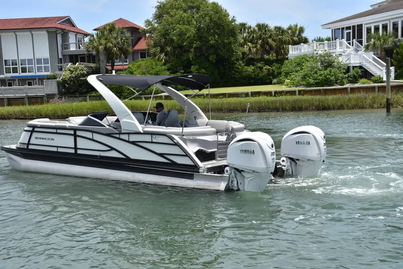 Slide: The Image of 2024 Bennington 27 QFB pontoon boat with Yamaha engines cruising near waterfront homes. - 32