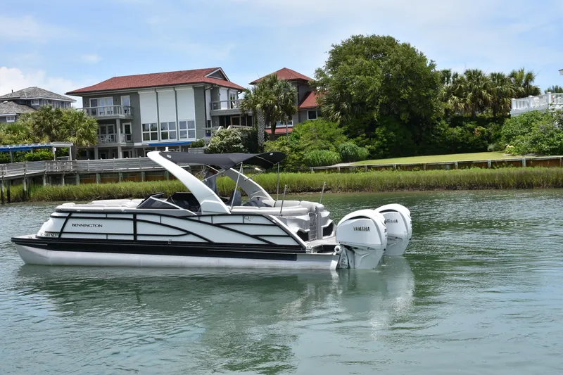 Slide: The Image of 2024 Bennington 27 QFB pontoon boat on calm water near waterfront homes. - 5