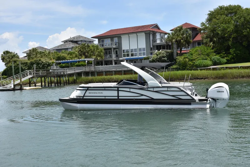 Slide: The Image of 2024 Bennington 27 QFB pontoon boat cruising near waterfront homes. - 7