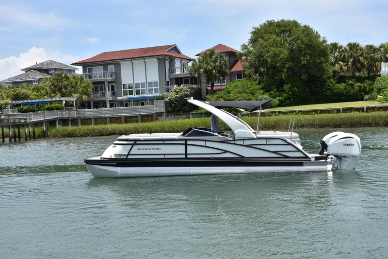 Slide: The Image of 2024 Bennington 27 QFB pontoon boat cruising near waterfront homes. - 8