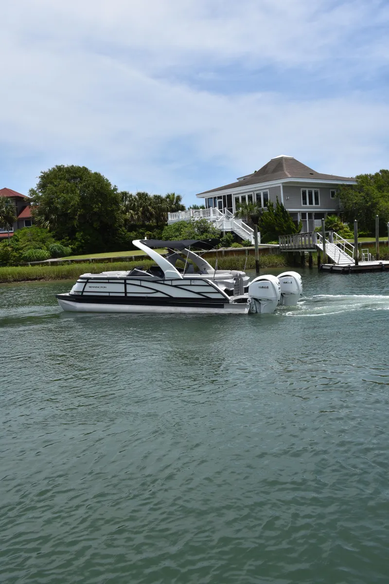 Slide: The Image of 2024 Bennington 27 QFB boat cruising on a serene waterway near a modern house. - 9