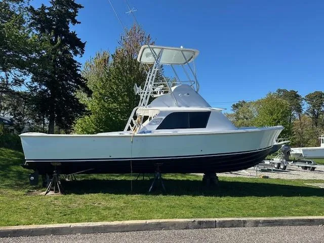 The Image of 1964 Bertram 31 Flybridge Cruiser on land, surrounded by trees and clear blue sky. - 0