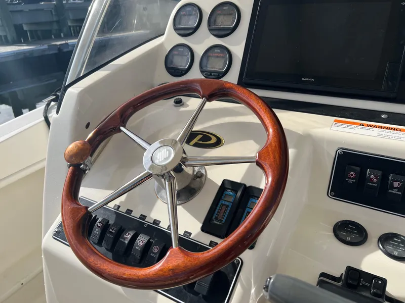 Slide: The Image of 2001 Pursuit 3070 Center Console boat dashboard with wooden steering wheel and control panel. - 14