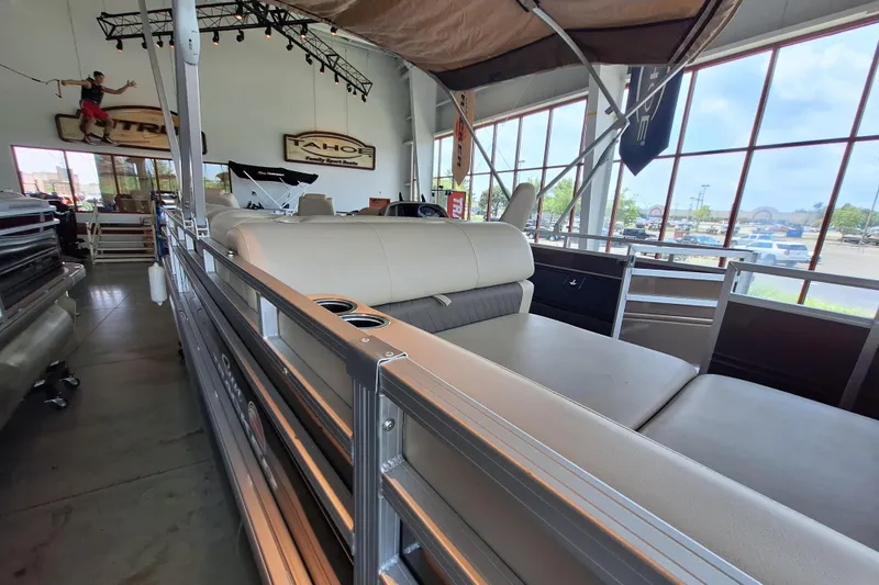 Slide: The Image of 2025 Sun Tracker Sportfish 24 XP3 pontoon boat interior in showroom, featuring beige seating. - 2