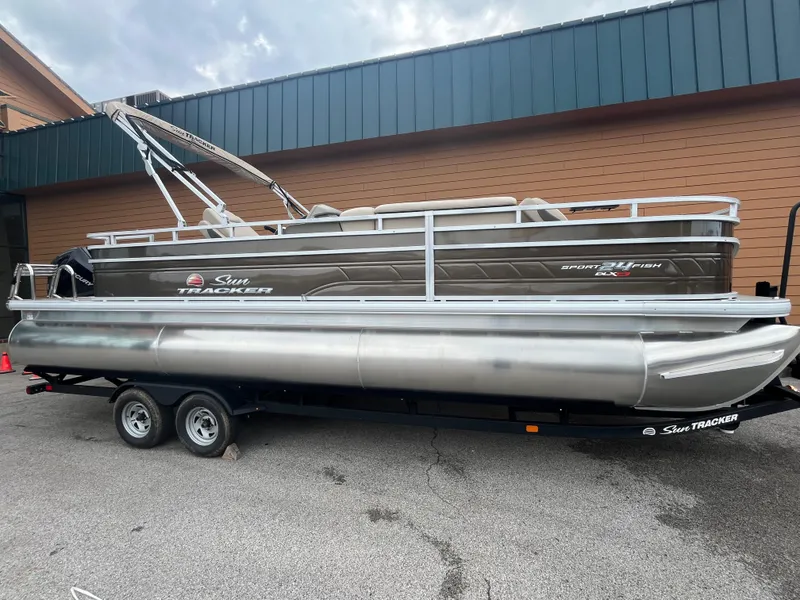 The Image of 2025 Sun Tracker Sportfish 24 XP3 pontoon boat on trailer, parked outdoors. - 0