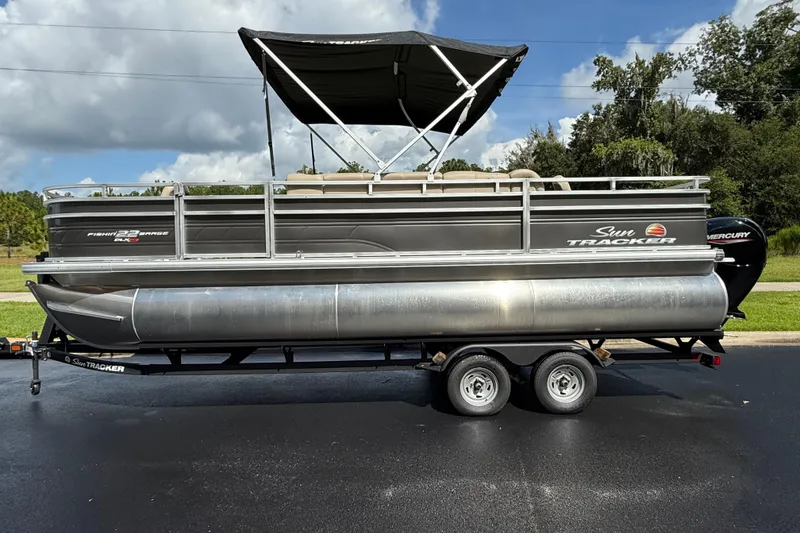 The Image of 2025 Sun Tracker Fishin' Barge 22 XP3 pontoon boat on trailer, parked outdoors. - 0