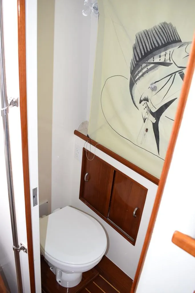 Slide: The Image of 1988 Rybovich Express Walkaround bathroom with wooden cabinets and nautical-themed shower curtain. - 11