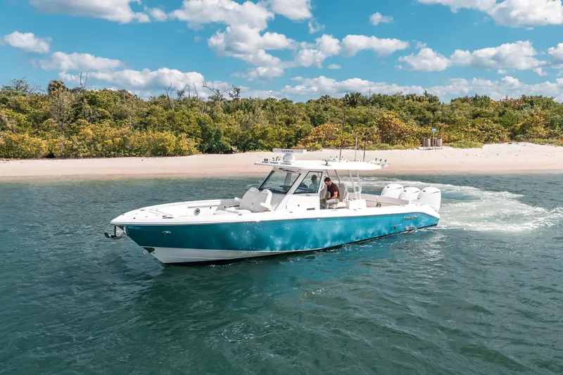 Slide: The Image of 2022 Everglades 395cc boat cruising near a sandy beach under a blue sky. - 1